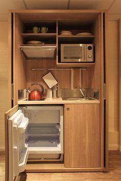 a small kitchen with an open refrigerator and microwave on the wall, next to a sink