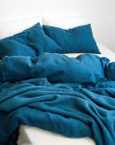 an unmade bed with teal blue sheets and pillows on it's side