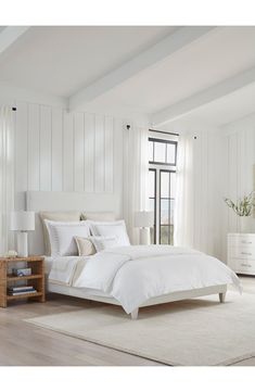 a white bed with pillows and blankets in a bedroom next to a window on top of a rug