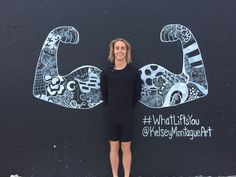 a woman standing in front of a black wall with white and black designs on it