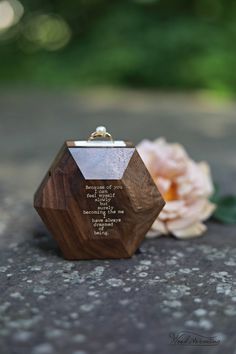 a wooden ring box sitting on top of a cement ground next to a pink flower