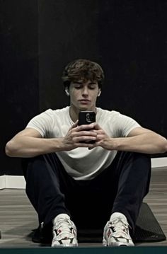 a young man sitting on the floor looking at his cell phone in front of him