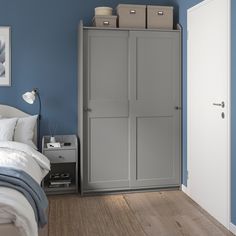 a bedroom with blue walls and white bedding has a gray armoire in the corner