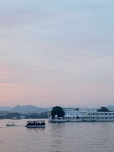 a large boat floating on top of a lake next to a tall white building in the distance