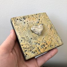 a hand holding a small square object with a heart on it