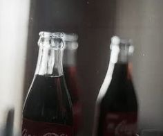 two coca - cola bottles sitting on top of a table next to a glass cup