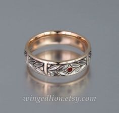 a wedding ring with two red stones in the center and leaves on it, sitting on a