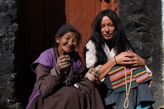 two women sitting next to each other in front of a door with beads on their hands