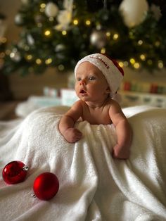 a baby laying on top of a bed next to a christmas tree