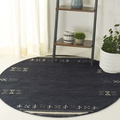 a black rug with white trim on the floor in front of a book shelf and potted plant