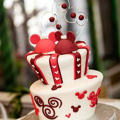 a red and white cake with mickey ears on top is sitting on a silver platter