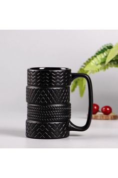 a black coffee mug sitting on top of a table next to a potted plant