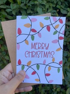 someone holding up a christmas card in front of some bushes and trees with the words merry christmas written on it