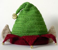 a crocheted green hat with red bottoms and bells on the top, sitting on a white surface