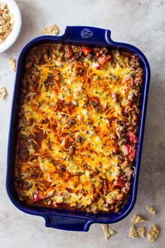 a casserole dish filled with meat, cheese and veggies next to a bowl of crackers