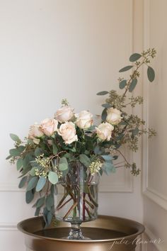 a vase filled with white roses on top of a metal table next to a wall