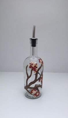 a glass bottle with red flowers on it sitting on a white counter top next to a toothbrush holder