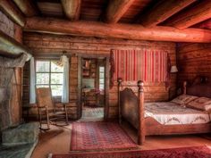 an old log cabin bedroom with a bed, rocking chair and rug on the floor