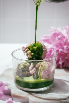 a person pouring green liquid into a glass bowl filled with flowers and cucumbers