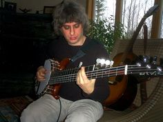 a man sitting in a chair playing a guitar and looking at the strings on his instrument