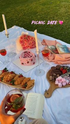 a table full of food and drinks on top of a white cloth covered picnic blanket