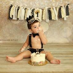 a baby is sitting on the floor with a cake in front of him and wearing a birthday hat