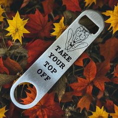 a bottle opener with the words take your top off on it in front of fall leaves