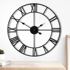 a large black clock on the wall next to a table with a potted plant