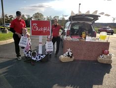 three people standing in front of a car with signs and stuffed animals on the ground