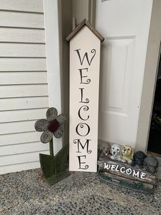 a welcome sign next to a door with a flower in front of it on the sidewalk