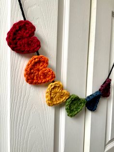 crocheted hearts are hanging on the front door with black string and red, yellow, green, orange, and blue yarn