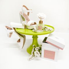 a green table topped with white shoes and flowers next to a box of perfumes