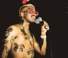 a man with tattoos on his chest holding a microphone and wearing a red nose ring