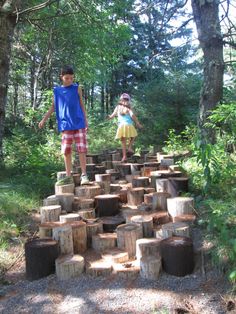 two children are playing in the woods with wooden stumps on each side of the path