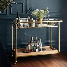 a bar cart with bottles and glasses on it in front of a dark blue wall