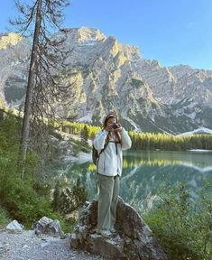 a woman taking a photo with her cell phone in front of a lake and mountains