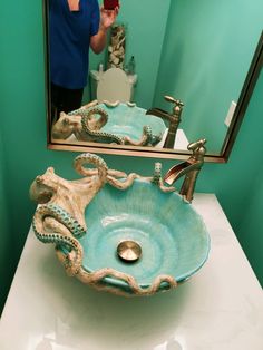 a bathroom sink with an octopus bowl on it and a person taking a photo in the mirror