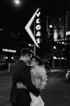 black and white photograph of a couple kissing in front of the vegas sign at night