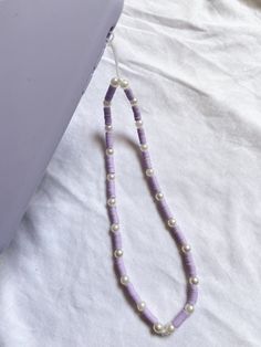 a purple and white beaded necklace laying on top of a bed next to a laptop