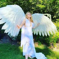 a woman dressed as an angel standing in the grass