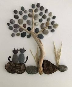 two cats sitting under a tree made out of pebbles and rocks on a white wall