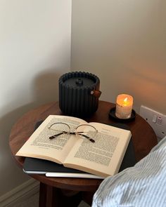 an open book sitting on top of a wooden table next to a candle and glasses