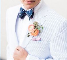 a man in a white suit with a blue bow tie and flower boutonniere