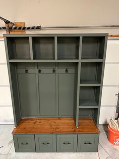 a large green bookcase with drawers and shelves in the middle, next to an orange bucket