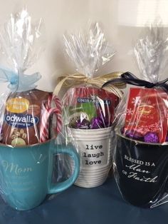 three coffee mugs wrapped in plastic wrap and filled with candy