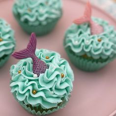 three cupcakes with blue frosting and pink icing on a pink plate