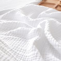 an unmade bed with white linens and a wooden tray on the floor next to it