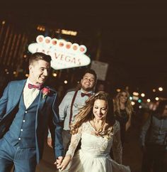 a bride and groom walking down the street at night with their wedding party in the background