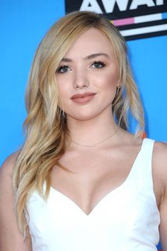 a woman with long blonde hair wearing a white dress at an awards event and posing for the camera