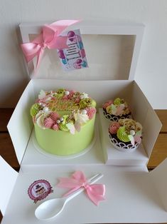 two cupcakes and a cake in a box with pink bows on the top